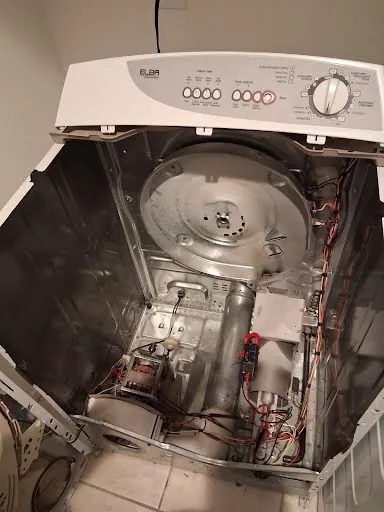Clothes dryer cabinet with the drum removed, exposing the motor and wiring