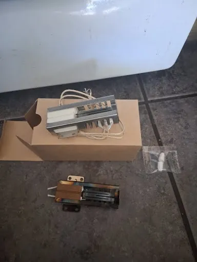 Replacement gas oven igniter in its box next to the worn original igniter