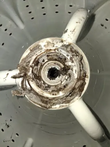 Top-load washer with the agitator removed, showing buildup around the drive