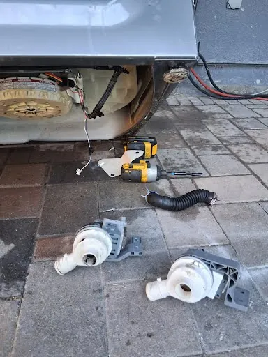Washing machine tipped up with the drain pump and hose removed for repair