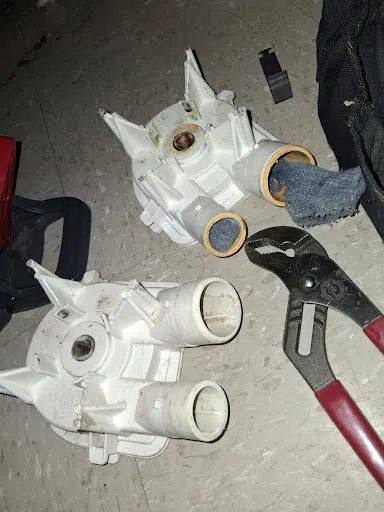 Old and new washing machine drain pumps on the floor next to pliers during a washer repair in Las Vegas